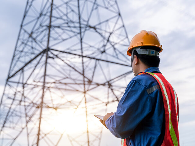 Electrical engineer wear safety clothes standing and watching at the electric power station to view the planning work by producing electricity at high voltage electricity poles.